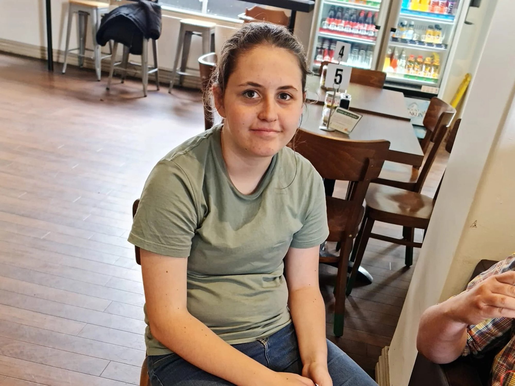 Young girl with brown hair wearing green tshirt sitting down